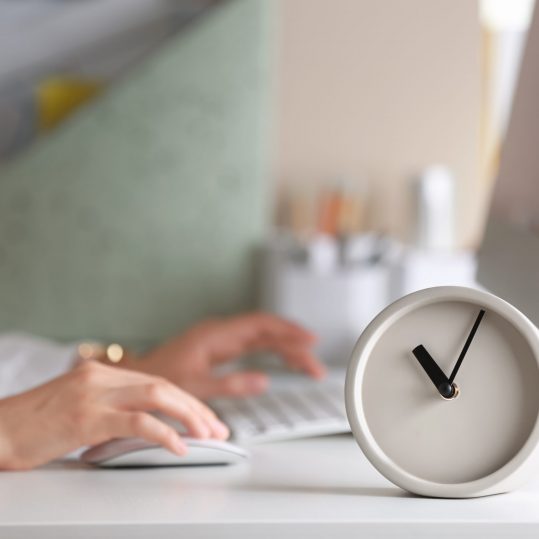 Alarm clock and blurred woman working on background. Time management