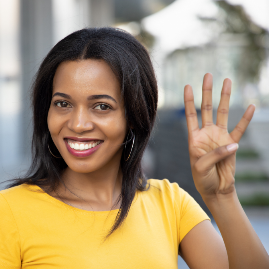Woman pointing, counting four finger; portrait of positive happy smiling black African woman pointing up 4 fingers for number four or 4 points concept; adult woman model